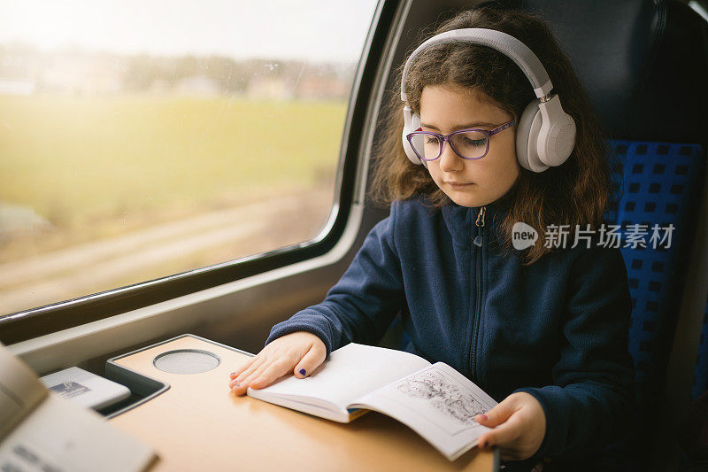 可爱的小女孩在火车上看书和听音乐