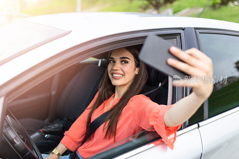 微笑的年轻女子与智能手机相机自拍在户外的汽车。假日和旅游概念——微笑的少女在车里用智能手机自拍