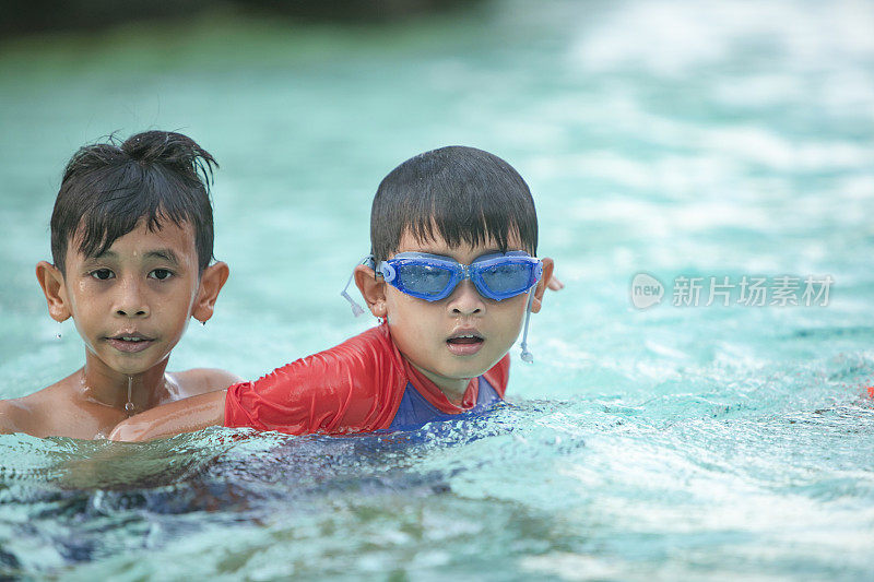 一群亚洲儿童在游泳池旁。他们在玩，享受着水