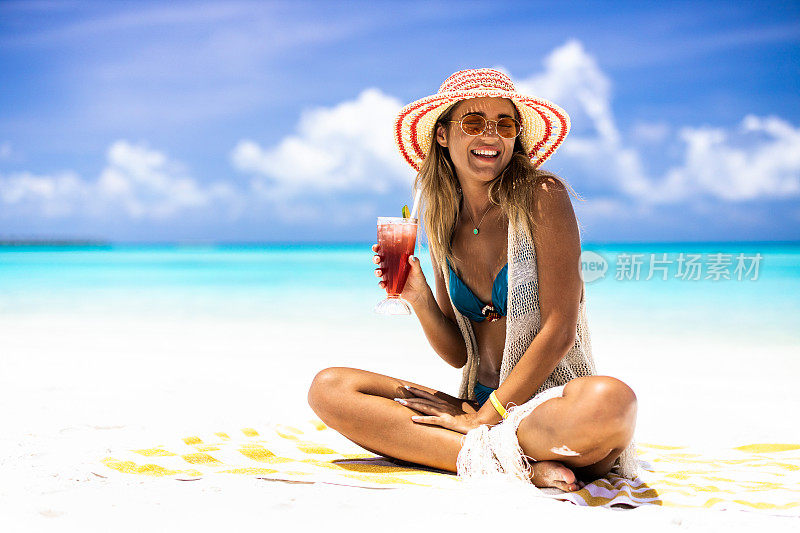 年轻快乐的女人在夏日的海滩上喝着鸡尾酒。
