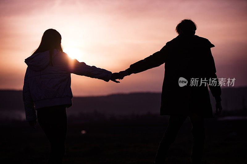一对十几岁的情侣在日落时分牵手一起在户外散步