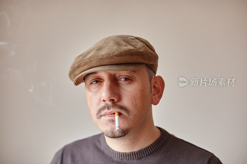 一名戴着帽子的白人男子在抽烟时带着怀疑的表情看着摄像机