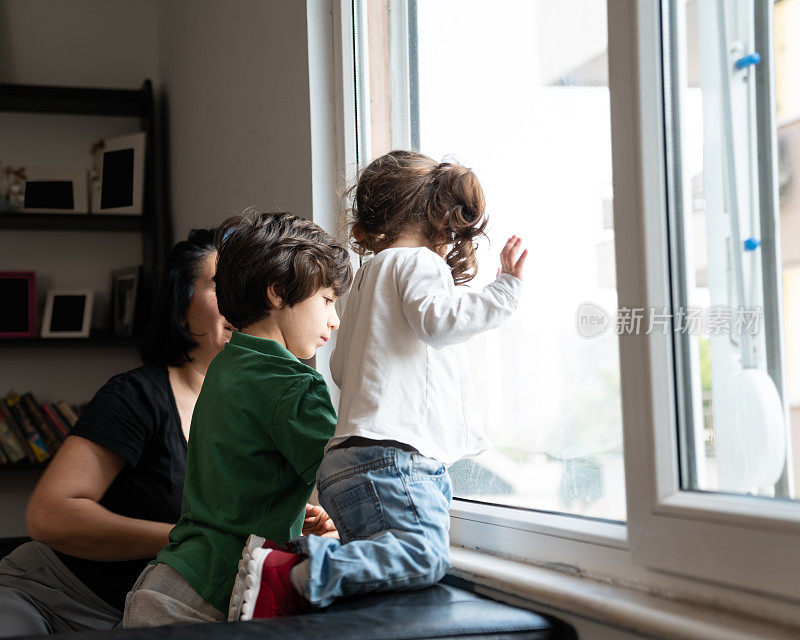 2019冠状病毒肺炎大流行封锁期间，母亲、儿子和女儿透过窗户看东西