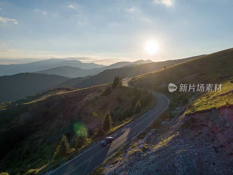 日落时分，无人机在山间柏油路上跟踪汽车。