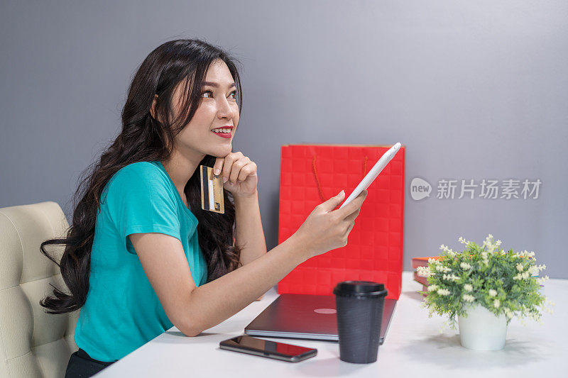 一个正在思考和使用数字平板电脑用信用卡进行网上购物的女人