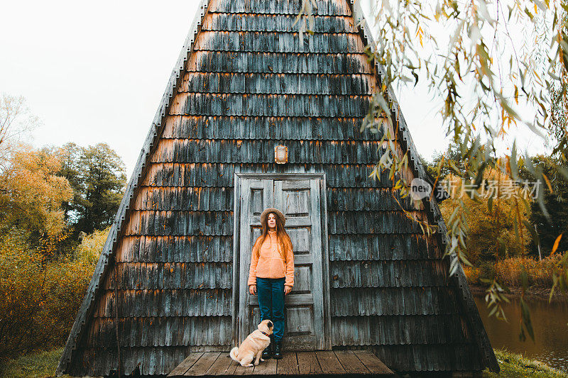 戴着帽子的女人和一只狗在美丽的三角形木屋旁享受秋天的羽衣甘蓝