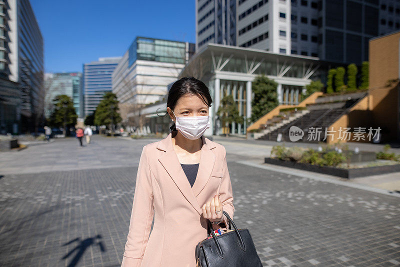 年轻的女商人戴着防护面具走在城市里