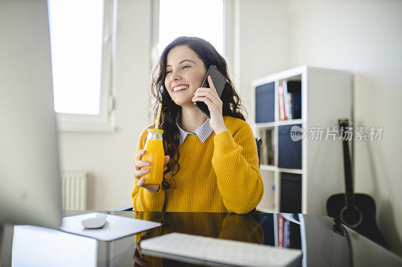 年轻的学生女孩喝果汁，在家里用手机