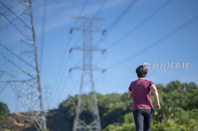 后视图亚洲华人中年妇女与运动服跑步在早上与电力线蓝色的天空背景