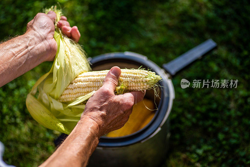 一名男子在室外的院子里剥新鲜的甜玉米