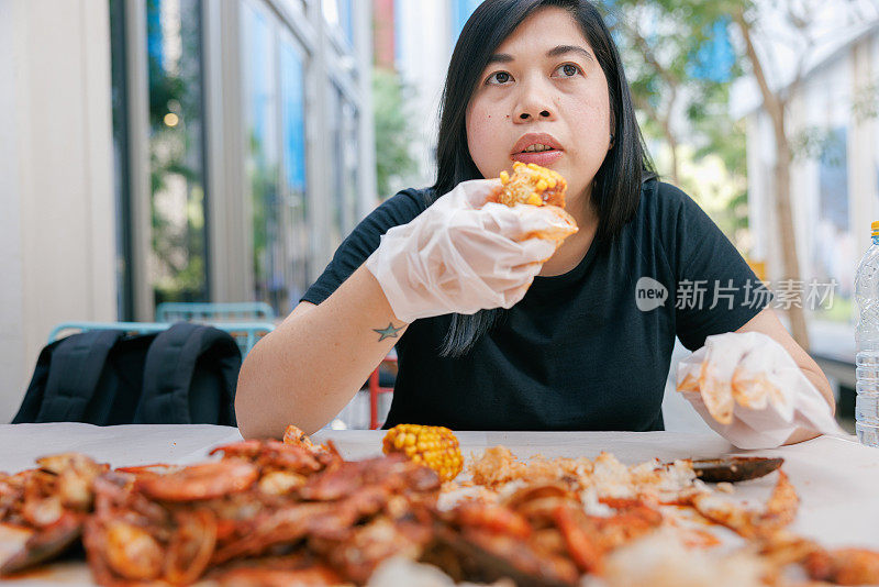 手戴手套，手拿甜玉米的女人，在路边餐馆吃海鲜饭