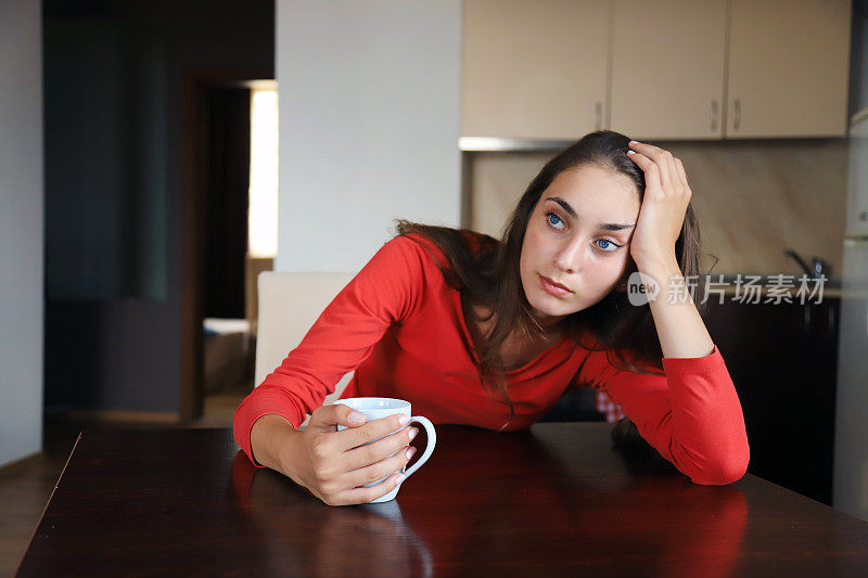 一个疲惫的女人在厨房端着一杯咖啡