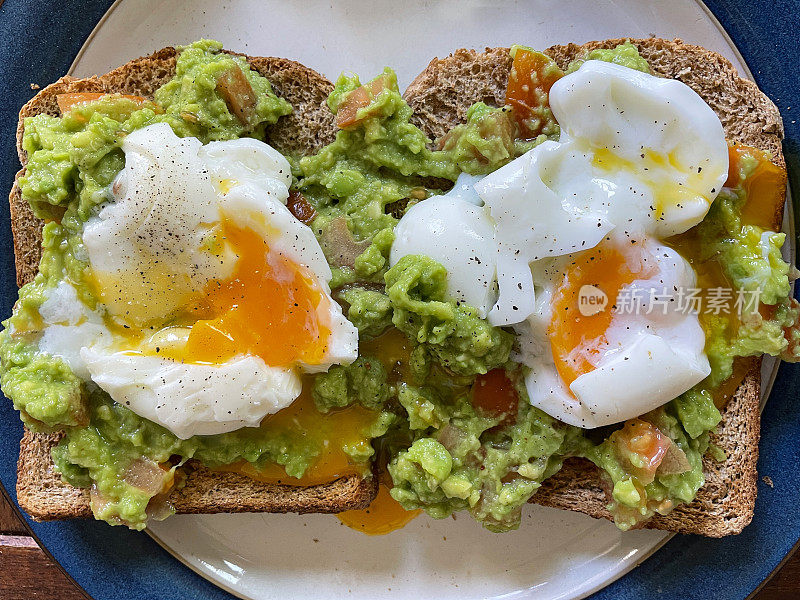 蓝色镶边的健康早餐盘的特写图像，两片全麦吐司上面涂着鳄梨酱和煮软的鸡蛋，溏心蛋黄，从高处俯瞰