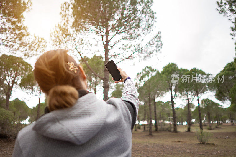 女性手拿智能手机在森林里自拍。