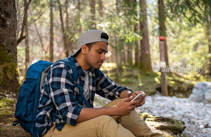 一名男子在森林里徒步旅行时，一边探索阿尔卑斯山，一边使用手机