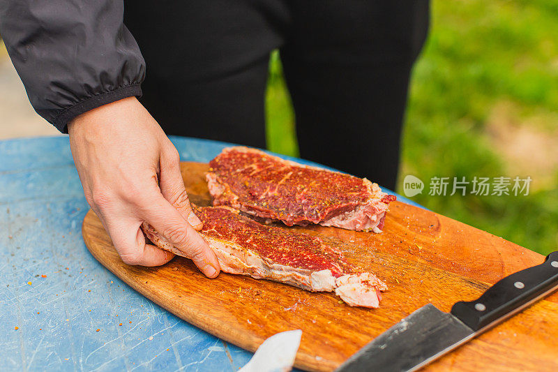 新鲜牛排。满足户外经验。晚餐在后院。木板上红肉。准备食物的过程。小牛肉。美味的小吃。户外用餐。盐和调味食品