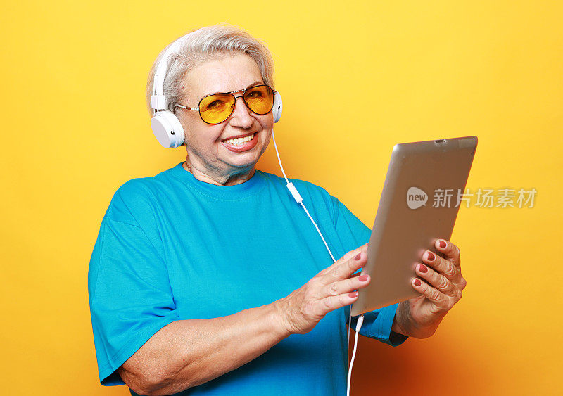 老妇人戴着耳机，黄色背景是平板电脑