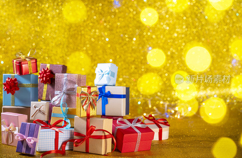 许多礼品盒堆叠作为圣诞礼品盒安排在金色闪闪的背景
