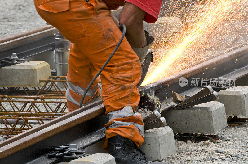一个穿橙色衣服的工人正在焊接一段铁路轨道