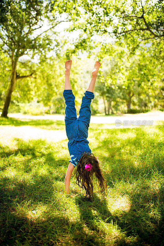 自由快乐的女孩做手倒立在一个草地公园