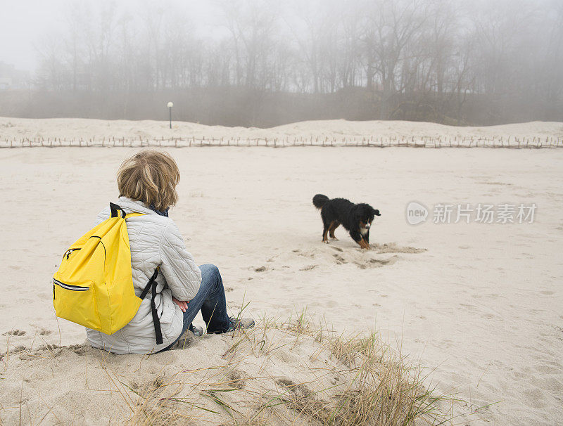 一个成熟的女人坐在波罗的海的沙滩上，和她的伯恩山地犬