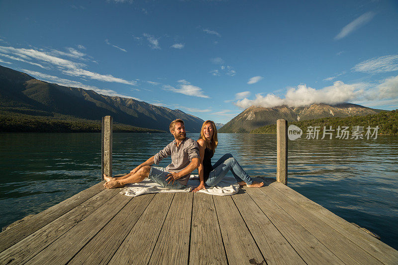 一对年轻夫妇背靠背坐在湖面上的防波堤上