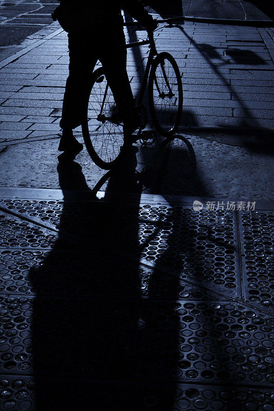 骑自行车的人独自在街角的蓝色夜晚的阴影