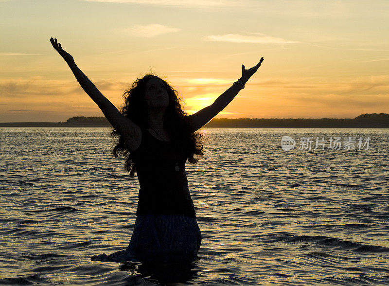 日落时女孩的剪影在海边的空中挥舞着手臂