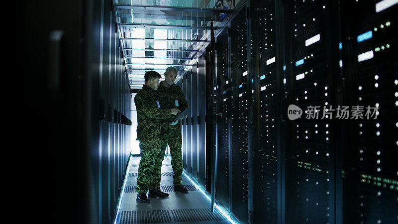 在数据中心，两名军人使用开放式服务器机架机柜工作。一个是军用版笔记本电脑。