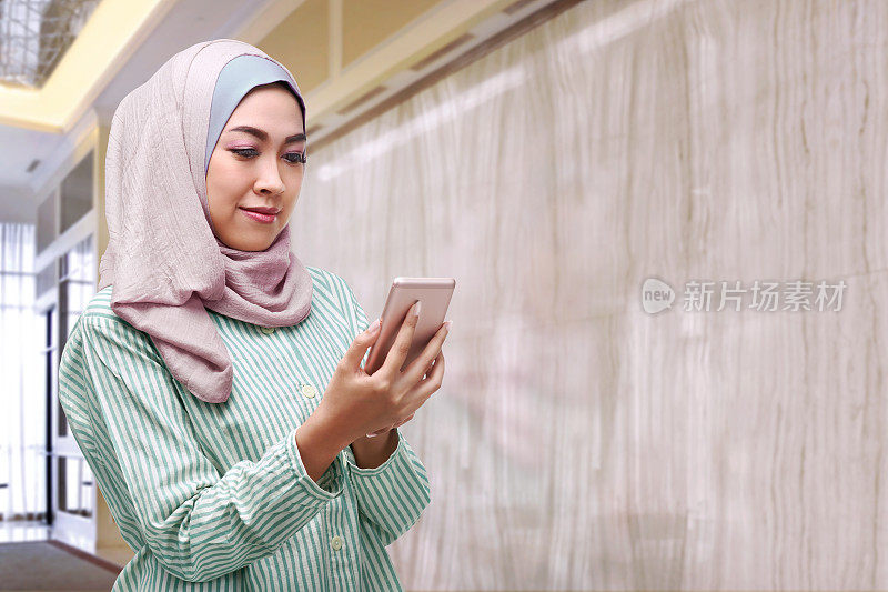 美丽的亚洲女人戴着头巾拿着智能手机