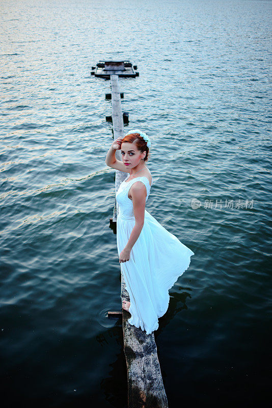新娘站在码头靠近水，穿着白色的裙子