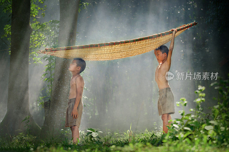 在泰国农村，两兄弟头顶竹船站在旁边。