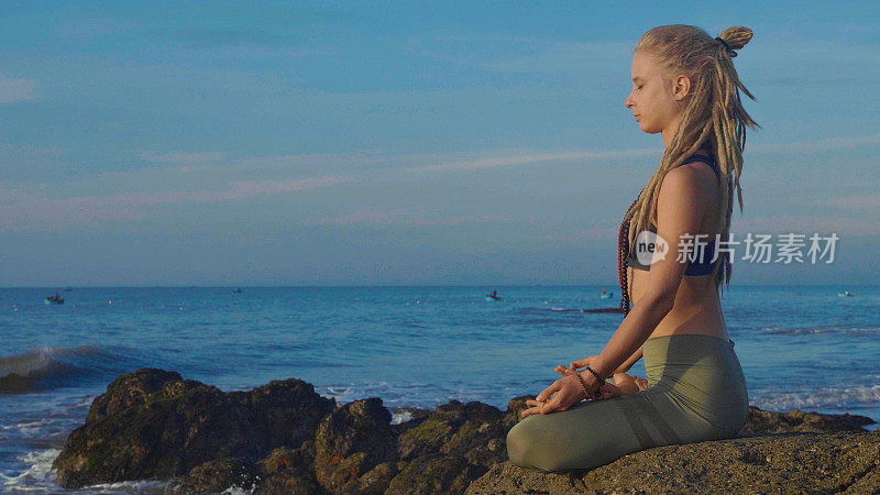 日落时做瑜伽。一个年轻女子在沙滩上冥想莲花姿势