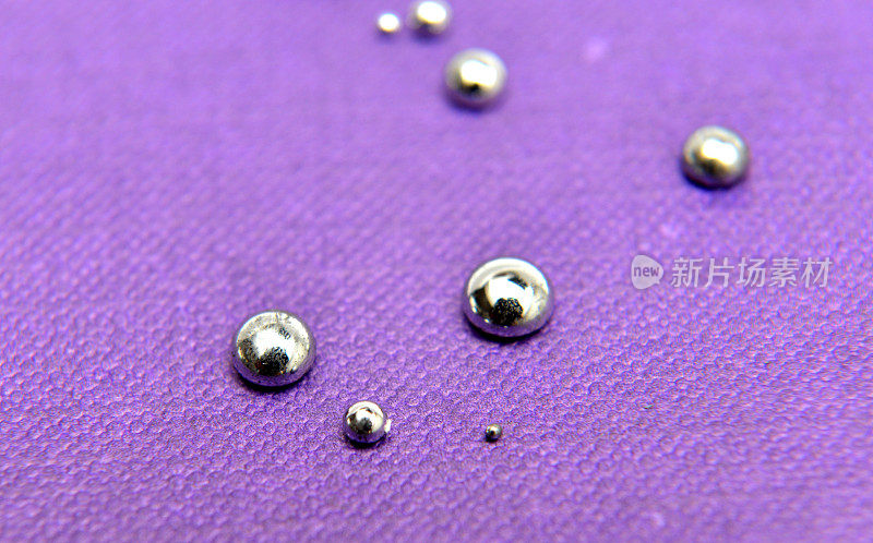 灰蒙蒙的水银滴在紫色的纸盒背景上，浅景深