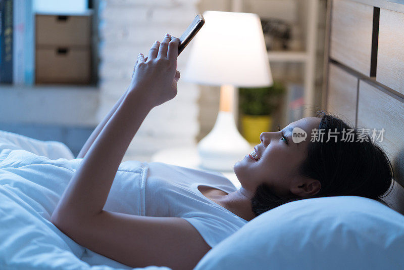 亚洲女性晚上睡觉前会在床上使用智能手机。手机成瘾的概念。