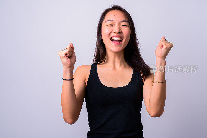 美丽的年轻中国女人的肖像，在白色的背景下举起双臂，看起来兴奋和快乐