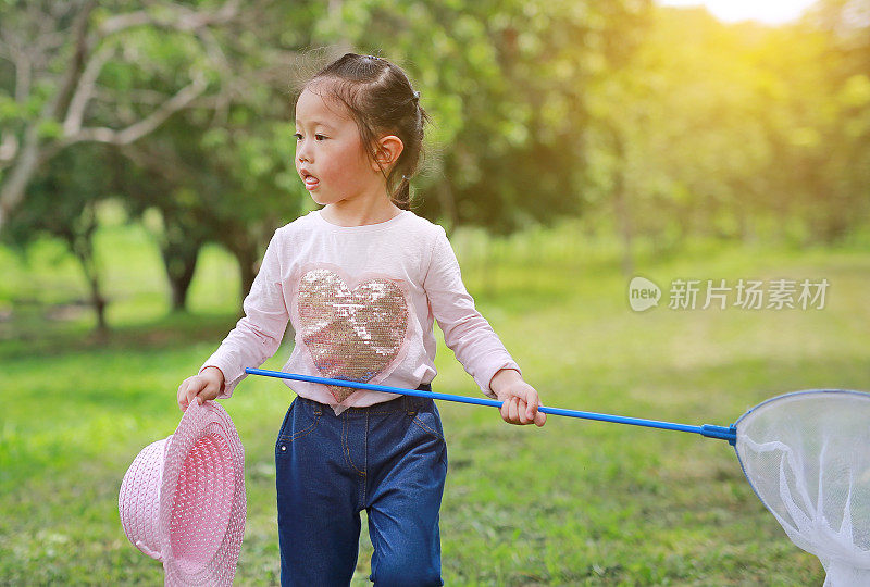 一个亚洲女孩在夏天用虫网在田野里玩。