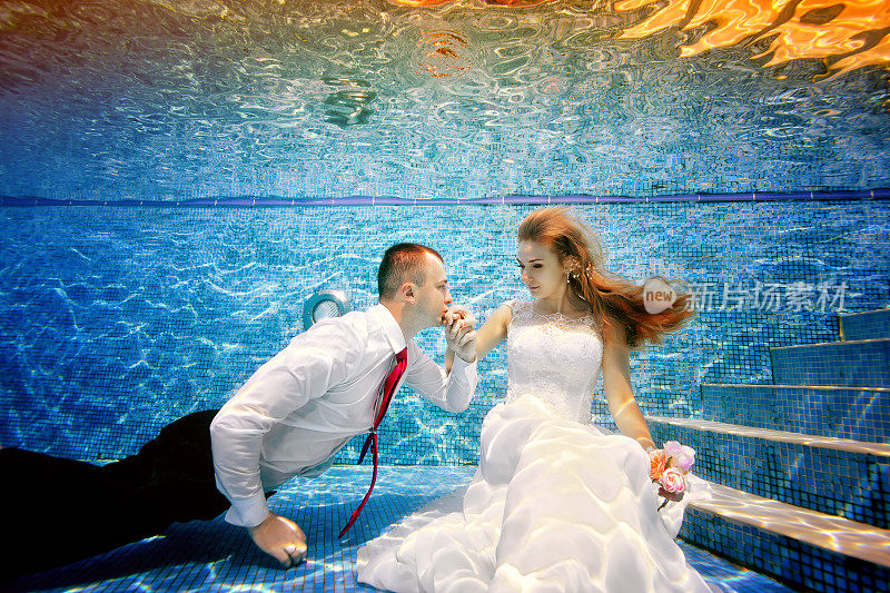 新郎在泳池里亲吻新娘的手。肖像。在水下拍摄