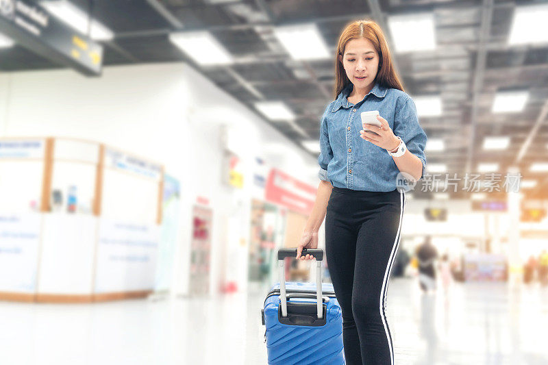 亚洲旅行者女性寻找航班在机场航站楼智能手机旅游概念