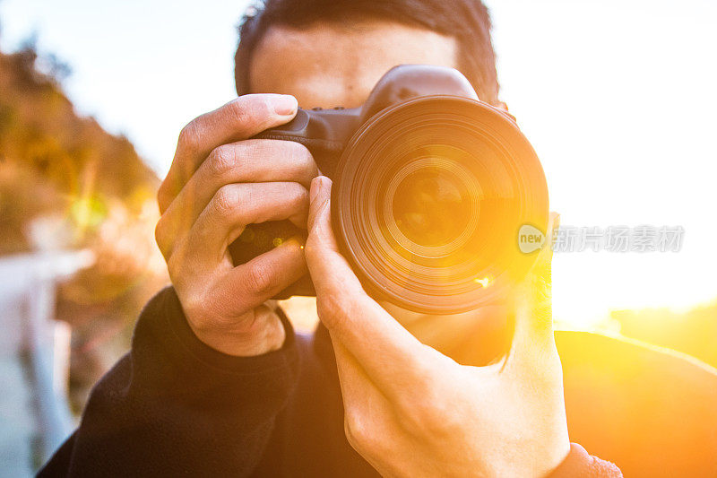 年轻男子在日落时用相机拍照的特写