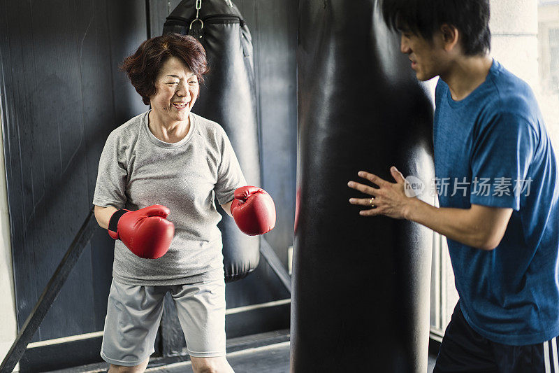 年长的成年女子训练在拳击馆与教练