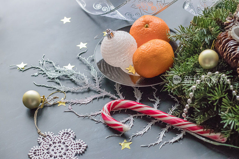 用松果、圣诞装饰品、彩带和冷杉枝制作的节日手工花环，在黑色背景上点缀新鲜的橘子