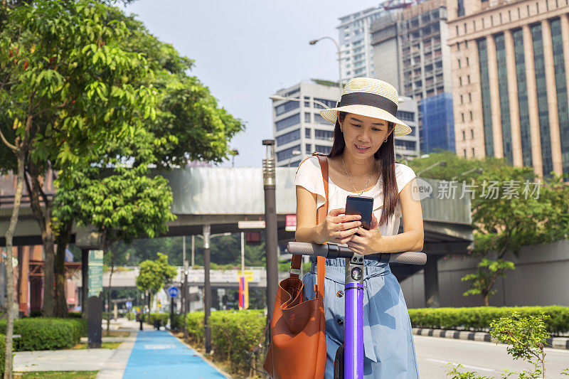 亚洲女性旅行者用手机发短信，在城市的自行车道上骑电动车