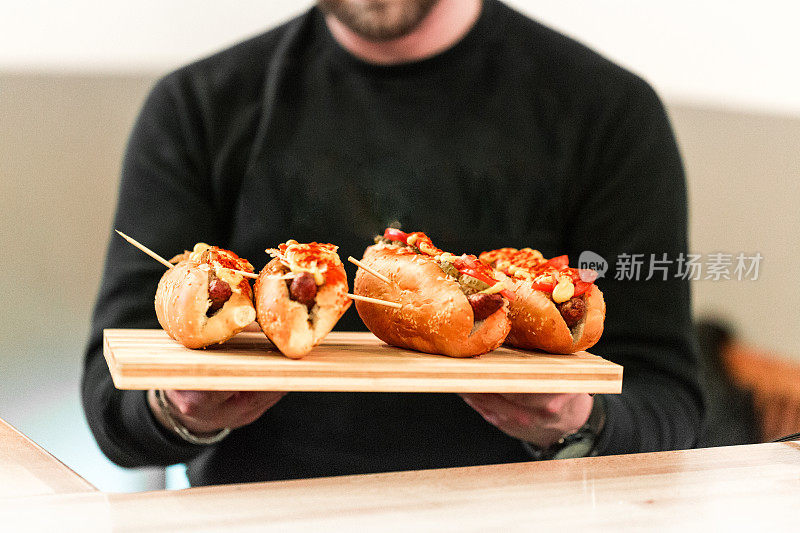 一个男人拿着装满芥末和西红柿的新鲜烤热狗在木板上