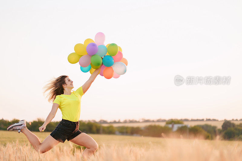 年轻女子在夏天的田野里拿着彩色气球