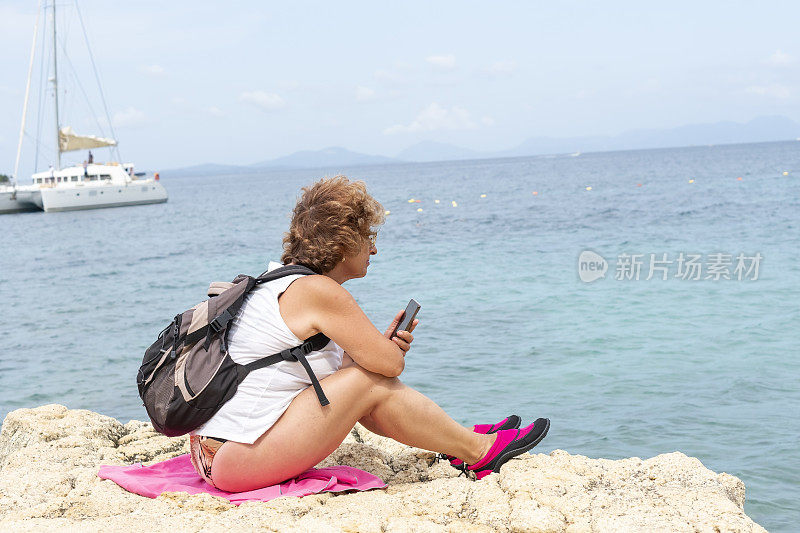 坐在海滩上玩智能手机的资深女性