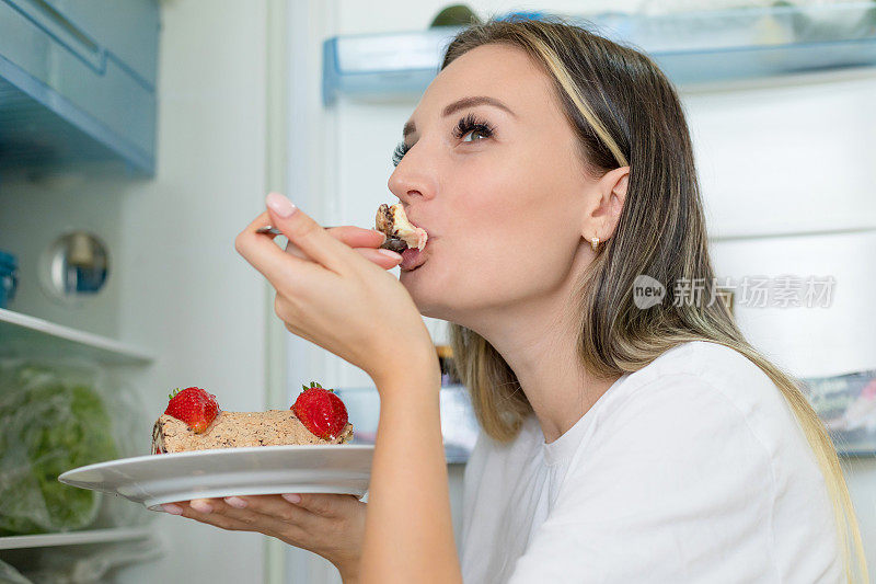 女人在打开的冰箱前吃不健康的蛋糕