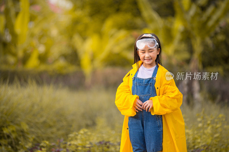 一个亚洲的中国女孩穿着雨衣和农家鞋在农场的草地上玩耍。