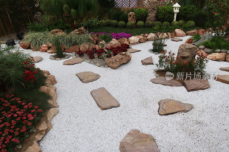白色的砾石覆盖的花园路径与踏脚石的图像，被植物边界与红色开花植物