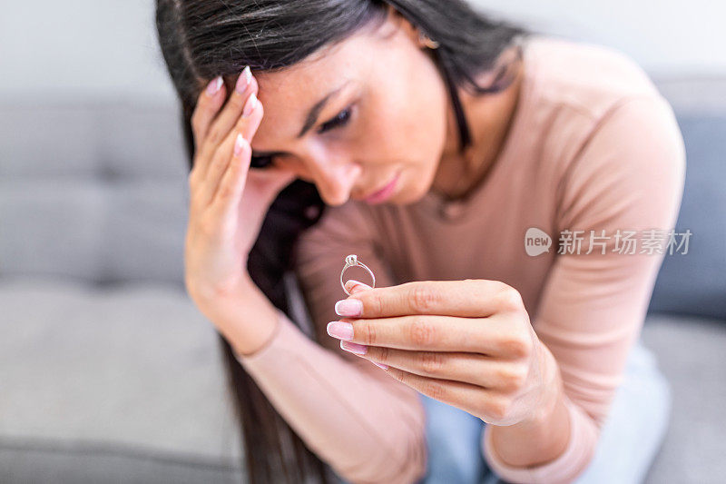 孤独、难过、体贴的离婚女人手里拿着金戒指，独自坐在家里，面对生活中的问题和关系的危机。破坏婚姻和离婚
